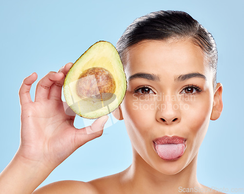 Image of This is how I glow. Studio portrait of an attractive young woman sticking out her tongue while posing with an avocado against a blue background.