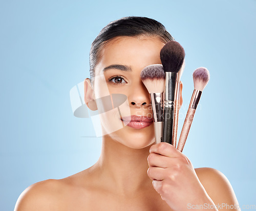 Image of Create magic with your wand. Studio portrait of an attractive young woman holding a collection of makeup brushes against a blue background.