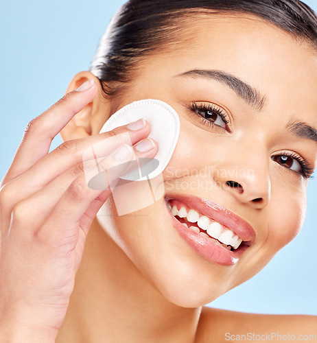 Image of Following all the steps in her skincare routine. Studio portrait of an attractive young woman using a cotton pad on her face against a blue background.