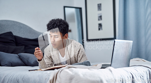 Image of 2020 had a slight change in plans. a young man writing in a notebook and using a laptop on his bed at home.