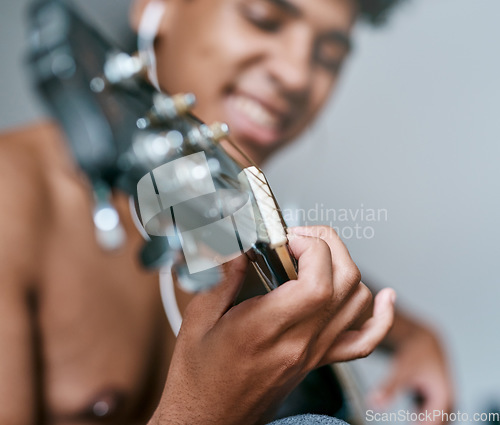 Image of Strike the chords that keep you smiling. a young man using earbuds while playing the guitar at home.