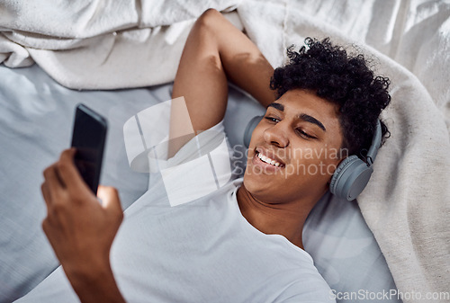 Image of All I need to survive lockdown. a young man using a smartphone and headphones while relaxing on his bed at home.