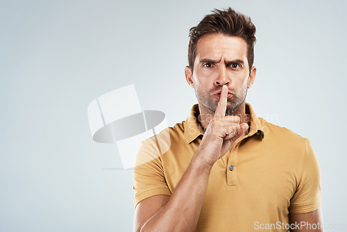 Image of Please keep it between us. Portrait of a carefree young man holding his finger on his mouth to keep quiet while standing against a grey background.