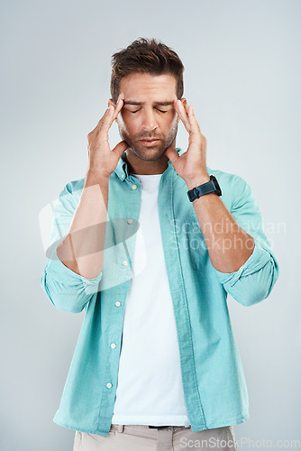 Image of Im not in the mood to think right now. Studio shot of a young man with an uncomfortable facial expression due to a headache while standing against a grey background.