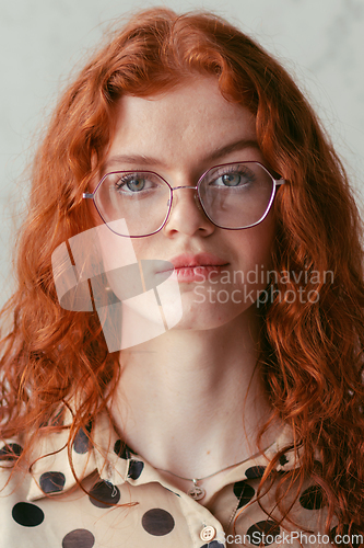 Image of A young entrepreneur with captivating orange hair is striking a confident pose in front of a stylish gray wall.