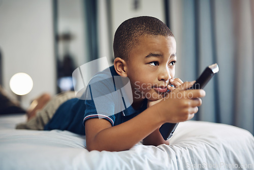 Image of Mom says I can only watch educational shows. a young boy using a remote control while lying on his bed.