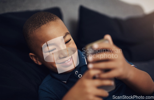 Image of I love playing games on my moms cellphone. a young boy using a cellphone while lying on his bed.