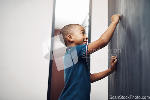 Image of Wait till you see how good my drawings are. a young boy writing on a blackboard at home.