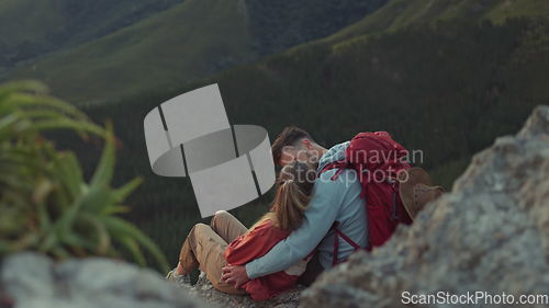 Image of Mountain, sunset or couple kiss to relax outdoors together on adventure in nature from back for view. Love, hiking or romantic man hugging woman sitting on cliff on camping holiday, vacation or break