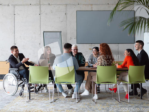 Image of A diverse group of business professionals, including an person with a disability, gathered at a modern office for a productive and inclusive meeting.