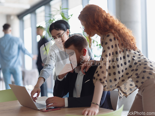 Image of A businessman engaging in a discussion about sales statistics with his two female colleagues while they examine the data on a laptop in a modern office setting