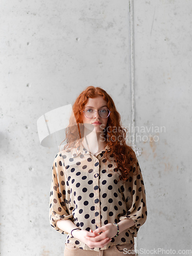 Image of A young entrepreneur with captivating orange hair is striking a confident pose in front of a stylish gray wall.