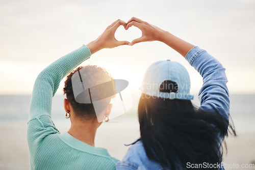 Image of Love, beach and lesbian couple with heart hands at sunset, summer holiday adventure or date together. Lgbt women, bonding and relax on ocean vacation with romance, pride and happy partner in nature.