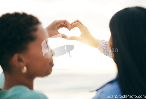 Image of Love, beach and lesbian couple with heart hands from back at sunset, summer holiday adventure or date together. Lgbt women, bonding and ocean vacation with romance, pride and happy partner in nature.