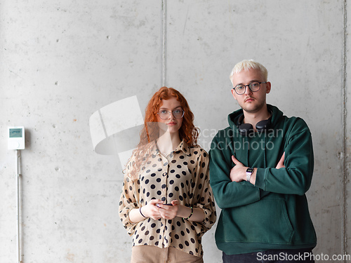 Image of A blonde man and a woman with orange hair standing together, their arms crossed, posing confidently in front of a gray wall, exuding a sense of style and professionalism.