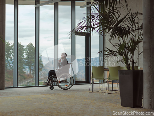 Image of A melancholic businessman in a wheelchair sitting with a sad expression, gazing through the window of a modern office, conveying a sense of solitude