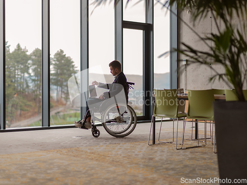 Image of A businessman with disability in a wheelchair using laptop in a modern office