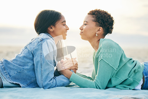 Image of Love, ocean and sunset, lesbian couple on blanket together, holding hands on sand and holiday adventure. Lgbt women, bonding and relax on beach vacation with romance, pride and happy lying in nature.