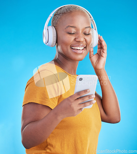 Image of Woman, phone and headphones for music, listening to audio and social media influencer on a blue background. Young african person on mobile, video streaming subscribe and radio or selfie in studio