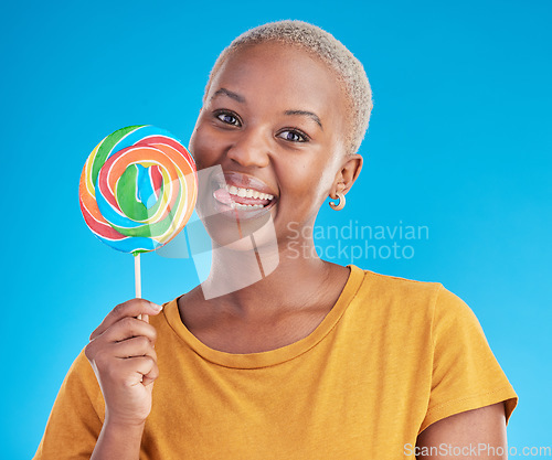 Image of Lollipop, portrait and a woman with candy in studio for sweets, rainbow and creative advertising. Happy black female person isolated on a blue background with sugar, freedom or happiness and tongue