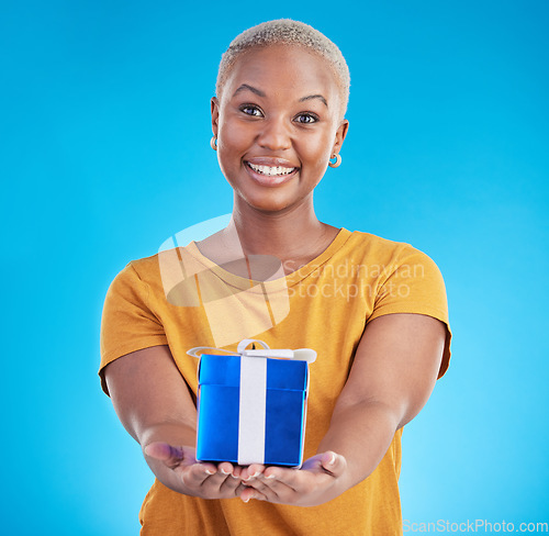 Image of Portrait, gift and happy black woman with giveaway in studio isolated on a blue background. Face, giving and person with present box for party, celebration or birthday package for offer of donation