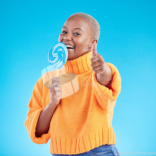 Image of Thumbs up, lollipop and black woman in portrait with candy in studio isolated on a blue background. African person, happy face and sweets, dessert and sugar food with like hand sign for excellence