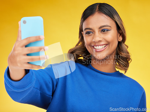 Image of Selfie, social media and smile with a woman on a yellow background in studio posing for a profile picture. Face, photograph and a happy young influencer indoor to update a status on her timeline