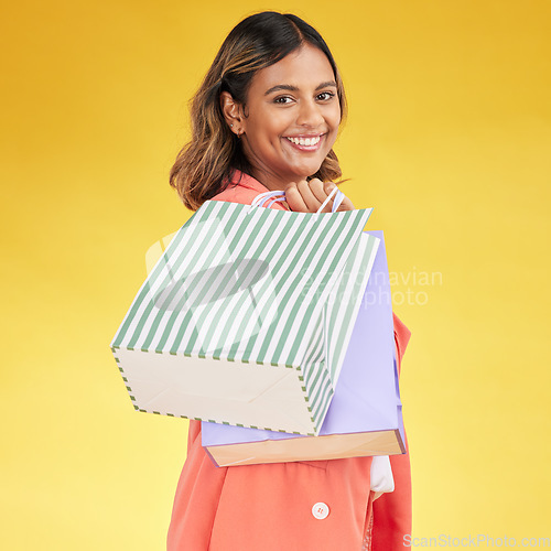 Image of Portrait, woman and smile with shopping bag in studio for fashion, retail deal or financial freedom on yellow background. Indian customer, gift bags and discount at boutique, store or sales promotion