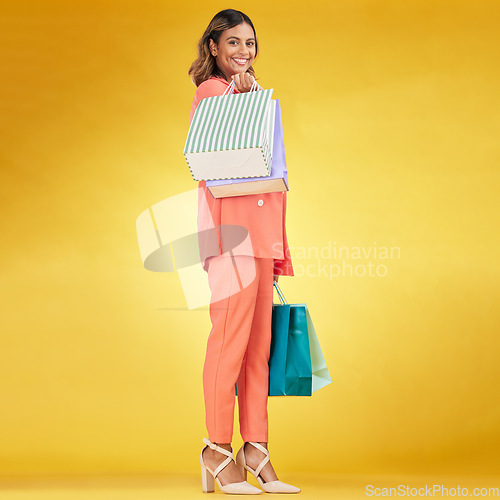 Image of Portrait, happy woman and shopping bag in studio for clothes, retail deal and financial freedom on yellow background. Indian customer, gift bags and discount from fashion store, sales and promotion