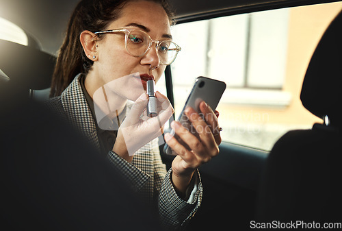 Image of Phone, lipstick and a business woman in a car to travel in the city for work while multitasking. Face, mobile and makeup with a young female employee in a taxi or cab as a passenger for transport