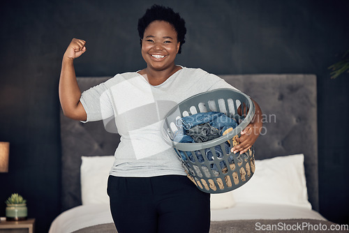 Image of Black woman, clothes in basket and champion, success in cleaning and bedroom with hygiene in portrait. Strong female cleaner, winner at housekeeping with smile, laundry and maintenance at home