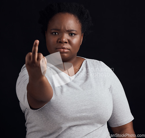 Image of Portrait, anger and black woman with middle finger, opinion and angry expression on a dark studio background. Face, female person and African model with hate sign, rude and frustrated with conflict