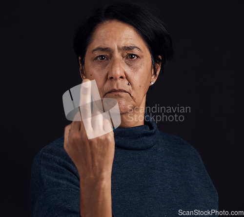 Image of Portrait, anger and senior woman with middle finger, opinion and expression on a black studio background. Face, female person and old model with gesture, rude and frustrated with problem and conflict