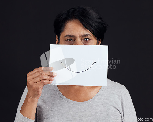 Image of Portrait, fake smile or depression and a mature woman in studio on a dark background with an expression. Abuse, anxiety and mental health with a female person looking brave to hide her emotions