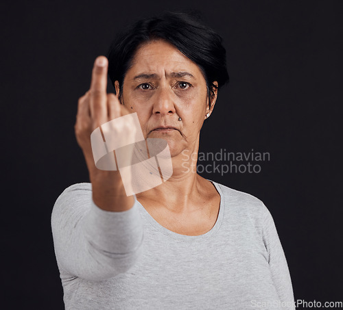 Image of Portrait, reject and senior woman with middle finger, opinion and angry expression on a black studio background. Face, female person or elderly model with hand gesture, rude and frustrated with anger