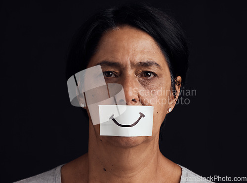 Image of Portrait, fake smile or abuse and a mature woman in studio on a dark background with an expression. Depression, anxiety and mental health with a female person looking brave to hide her emotions