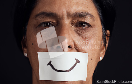 Image of Portrait, smile or anxiety and a mature woman in studio on a dark background with a fake expression. Depression, abuse and mental health with a female person looking brave to hide her emotions