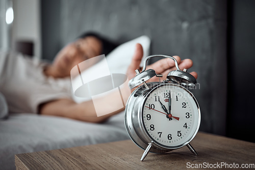 Image of Alarm, sleeping and a hand with a clock for awake, oversleep or tired in the bedroom of a home. House, ring and a closeup of a person or woman in bed for snooze, rest or waking up lazy in a house