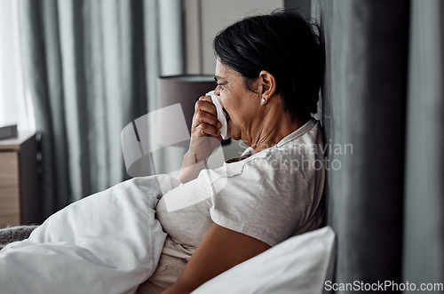 Image of Sick, tissue and elderly woman in bed blowing nose, flu or viral infection in her home. Allergies, bacteria and senior female sneezing, coughing or sore throat in a bedroom with virus or covid