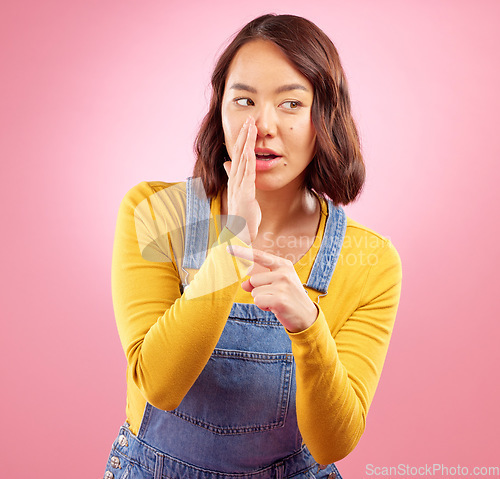 Image of Whisper, hand pointing and asian woman in studio with gossip, drama or hush news on pink background. Secret, did you know and Japanese female with emoji for confidential, privacy or coming soon promo