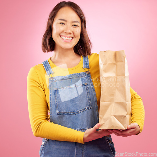 Image of Woman, paper bag and studio portrait with shopping, discount or groceries with smile by pink background. Japanese gen z girl, retail customer and package for product, sale and excited for cheap deal