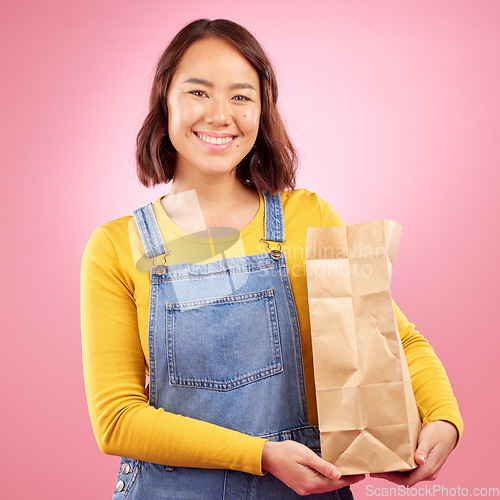 Image of Woman, paper bag and studio portrait for grocery shopping, discount or choice with smile by pink background. Japanese gen z girl, retail customer and package for product, sale or happy for cheap deal