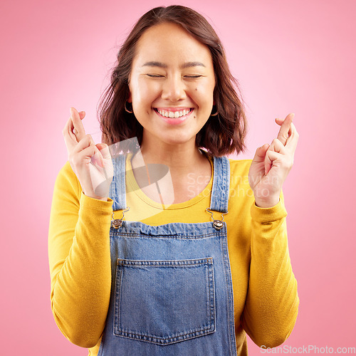 Image of Asian, woman and fingers crossed for hope in studio, pink background or praying for luck. Happy model wish with hands for bonus, promotion or winning giveaway for emoji, competition prize and lottery