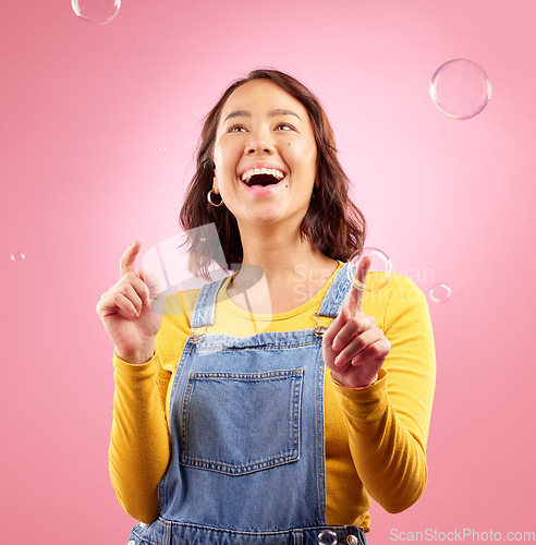 Image of Happy, woman and play with bubbles in studio, pink background and excited to celebrate freedom. Asian female model pop liquid soap bubble for fun, entertainment and burst of magic, color and creative