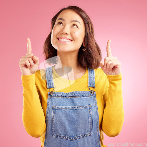 Image of Happy, pointing and young woman in a studio for presentation for marketing, promotion or advertising. Smile, confident and Asian female model with showing finger gesture isolated by a pink background