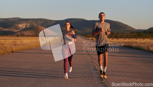 Image of A handsome young couple running together during the early morning hours, with the mesmerizing sunrise casting a warm glow, symbolizing their shared love and vitality