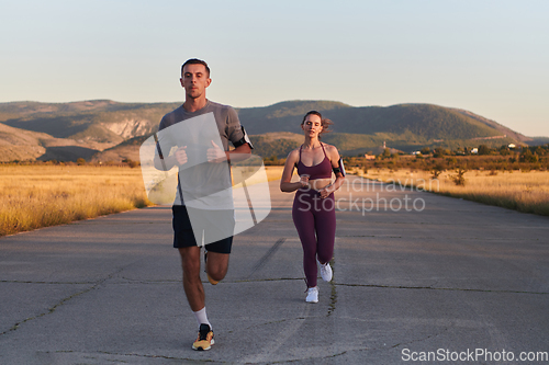 Image of A handsome young couple running together during the early morning hours, with the mesmerizing sunrise casting a warm glow, symbolizing their shared love and vitality