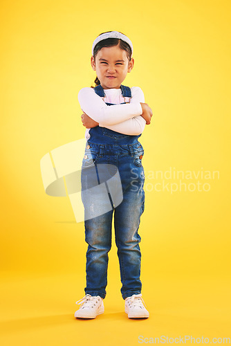 Image of Arms crossed, angry and portrait of girl child in studio with bad, attitude or behavior problem on yellow background. Frown, face and asian kid with body language for no, frustrated or tantrum emoji