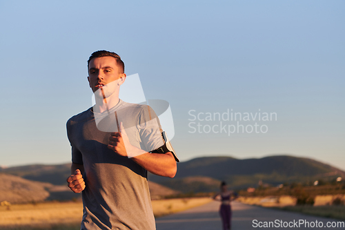 Image of A handsome young couple running together during the early morning hours, with the mesmerizing sunrise casting a warm glow, symbolizing their shared love and vitality