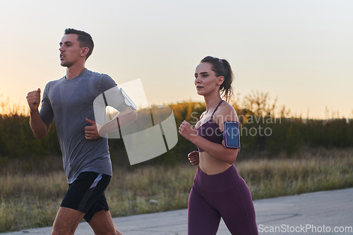 Image of A handsome young couple running together during the early morning hours, with the mesmerizing sunrise casting a warm glow, symbolizing their shared love and vitality